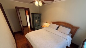Un dormitorio con una cama de madera, una mesita de noche, una lámpara, un ventilador de techo y un armario verde.