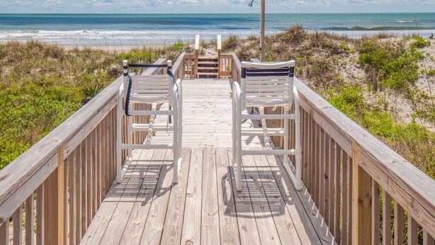 A wooden boardwalk leading to beach chairs overlooking the ocean.