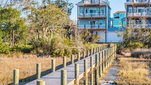A wooden boardwalk leading to beachfront properties with multiple stories and balconies. - Happily Ever After by Topsail Realty (Holly Ridge)