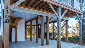 A spacious covered outdoor area with wooden beams and a concrete floor, likely part of a building's structure. - Happily Ever After by Topsail Realty (Holly Ridge)