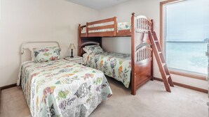Un dormitorio con dos literas, una mesita de noche con lámpara y una ventana con persianas.