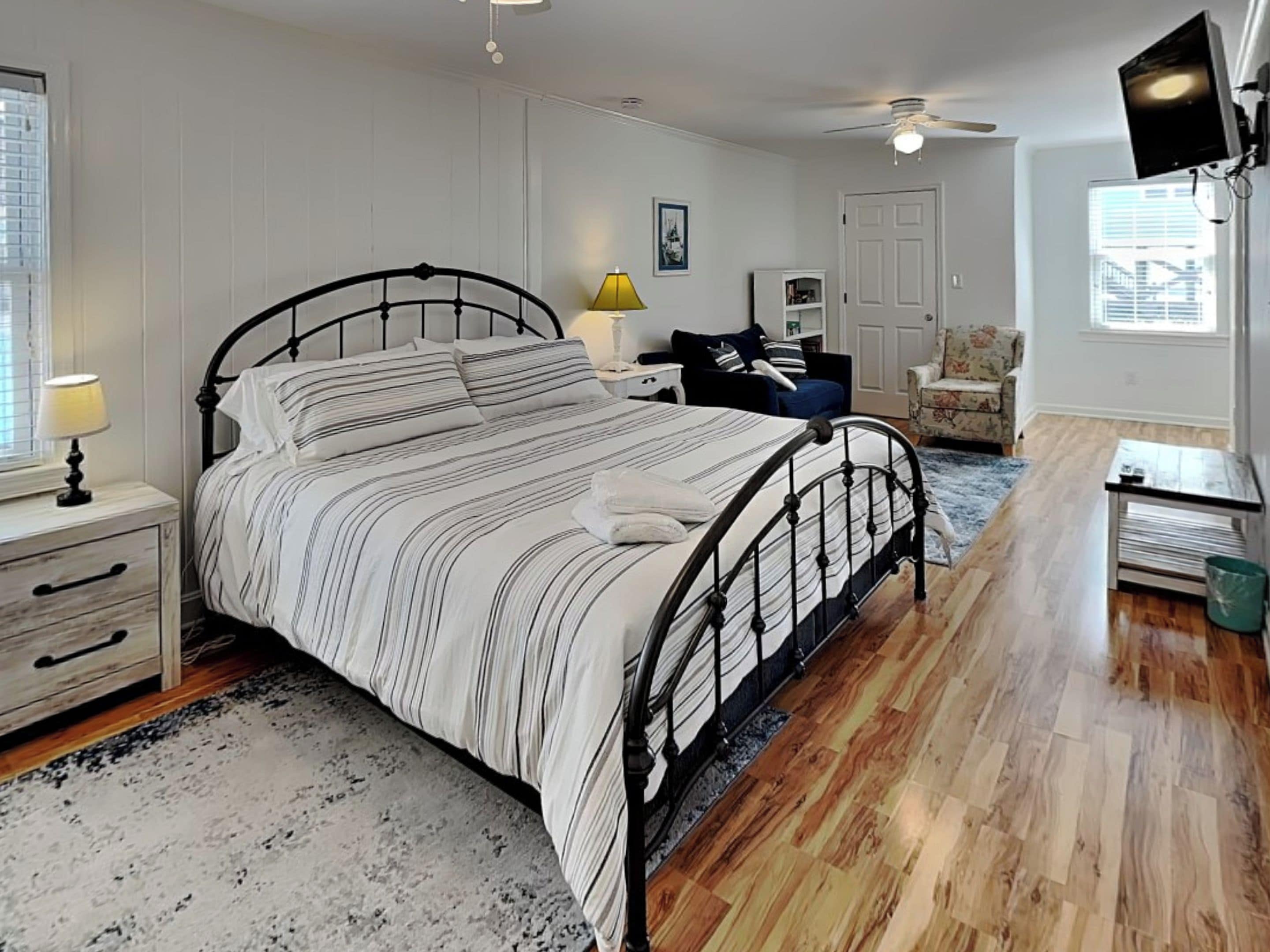 A bedroom with a bed, bedside tables, a chair, a desk, a television, and a ceiling fan.