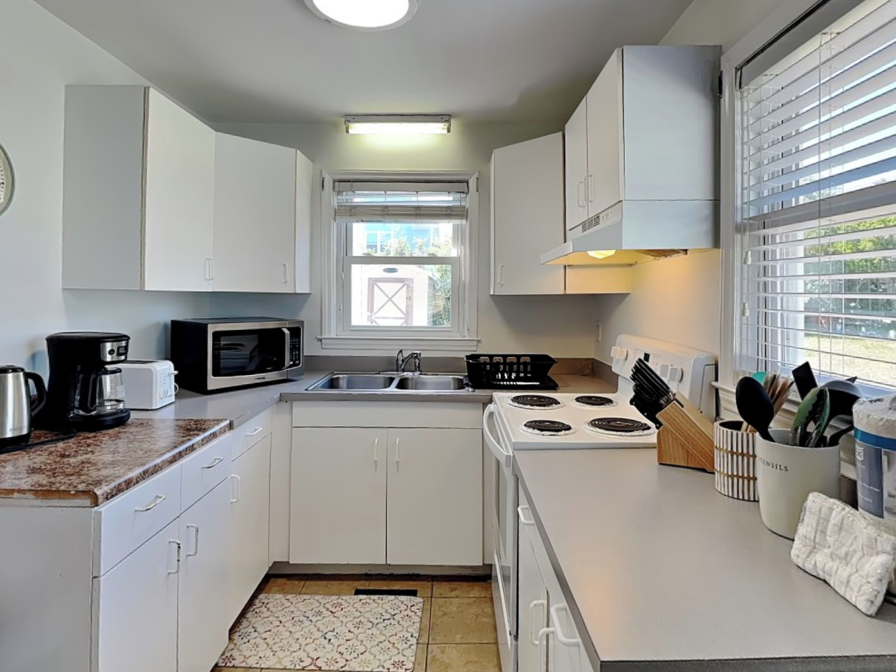A compact kitchen with white cabinets, a microwave, a stove, and a sink.