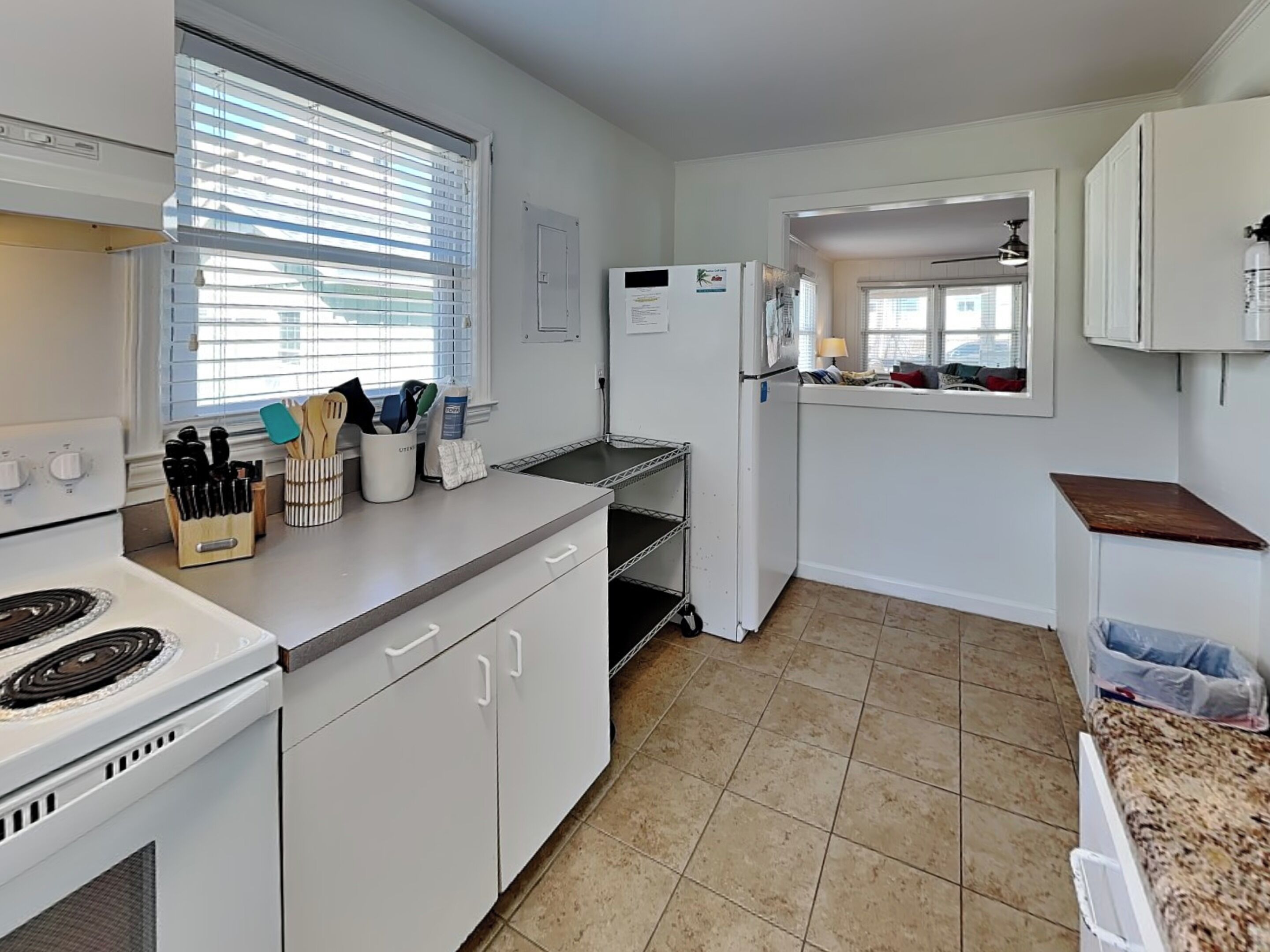 A kitchen with white cabinets, a stove, a sink, and a window with blinds.