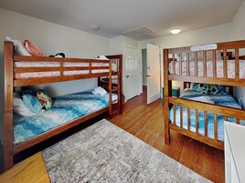 Quarto com beliches, um tapete e uma porta que dá para outro cômodo.