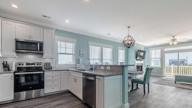 A modern kitchen with white cabinets, stainless steel appliances, and a large island. - Strand Bungalow by Topsail Realty (Holly Ridge)