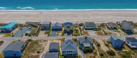 An aerial view of a coastal residential area with houses, a beach, and a clear sky.