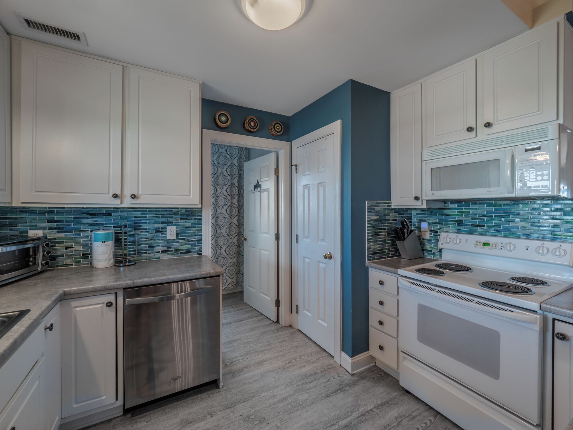 A kitchen with white cabinets, a stainless steel dishwasher, a white stove, and a microwave.
