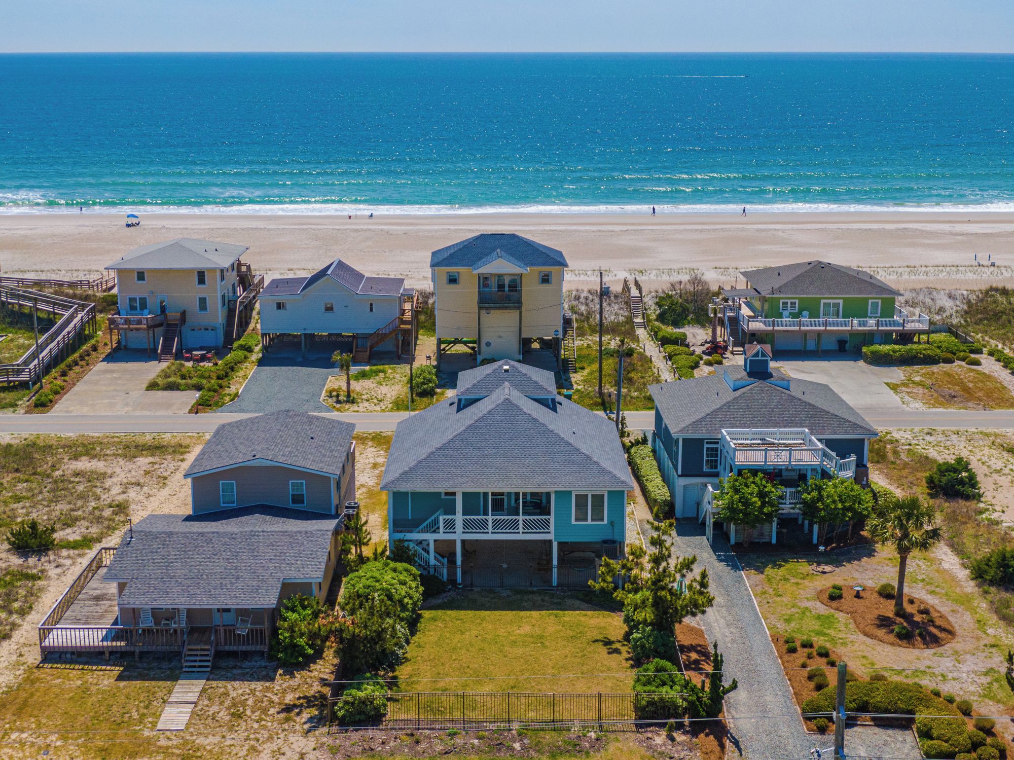 A coastal residential area with houses near the beach, featuring a mix of single and multi-story buildings, some with balconies and others with attached porches.
