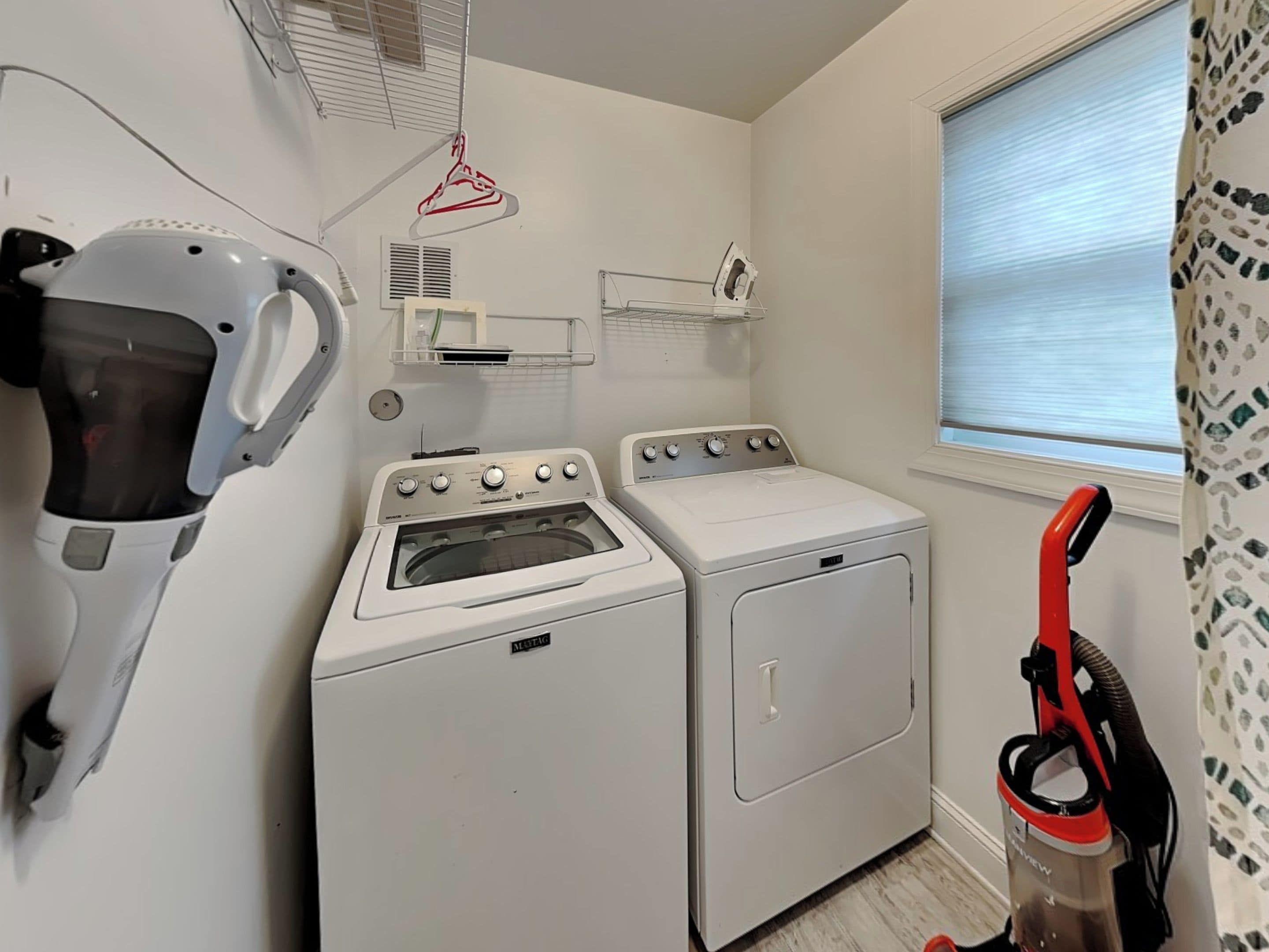 Une buanderie équipée d’un lave-linge à chargement frontal, d’un sèche-linge, d’un fer à vapeur et d’un étendoir.