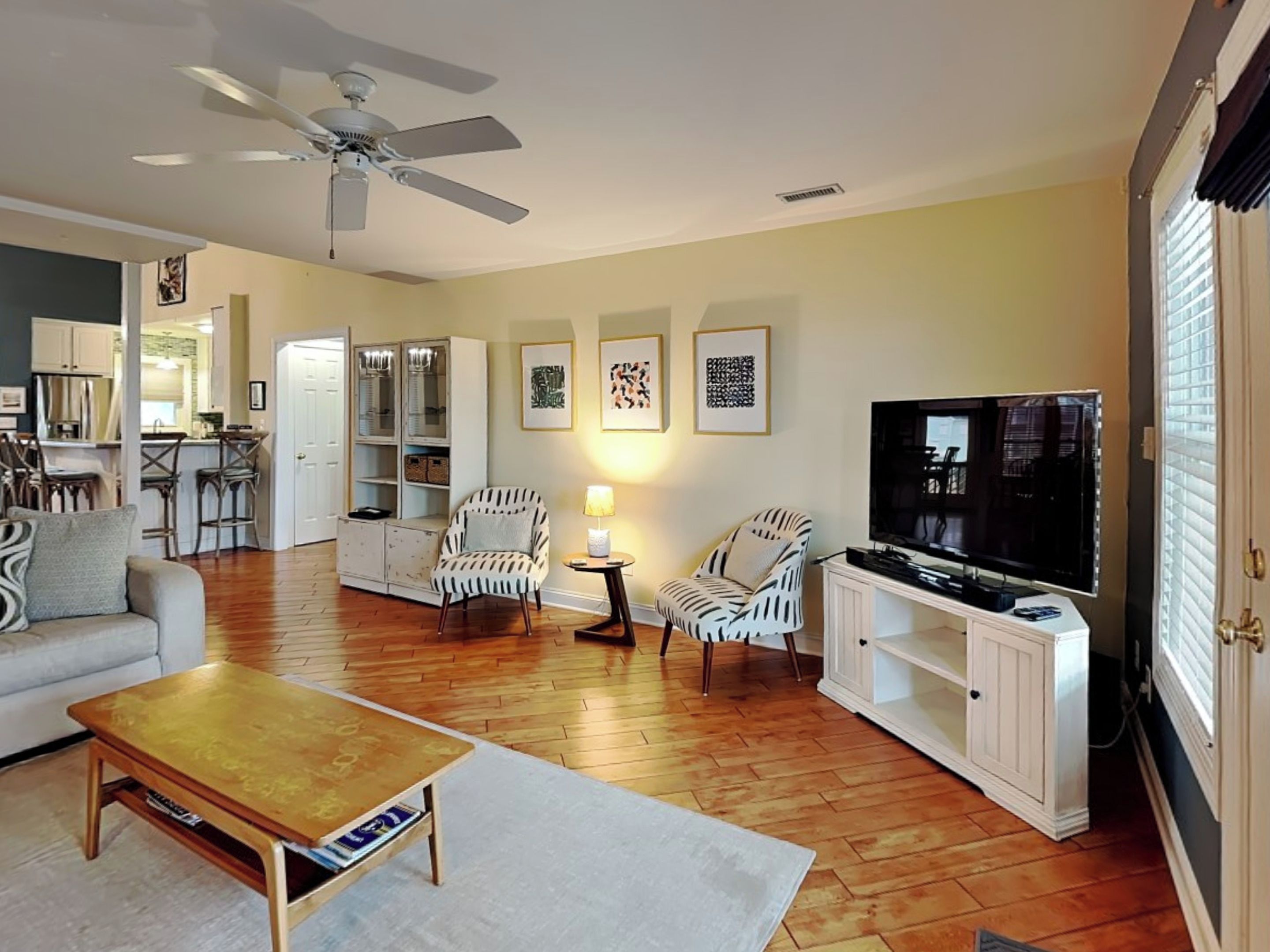 A living room with a sofa, armchairs, a coffee table, a TV, and a ceiling fan.