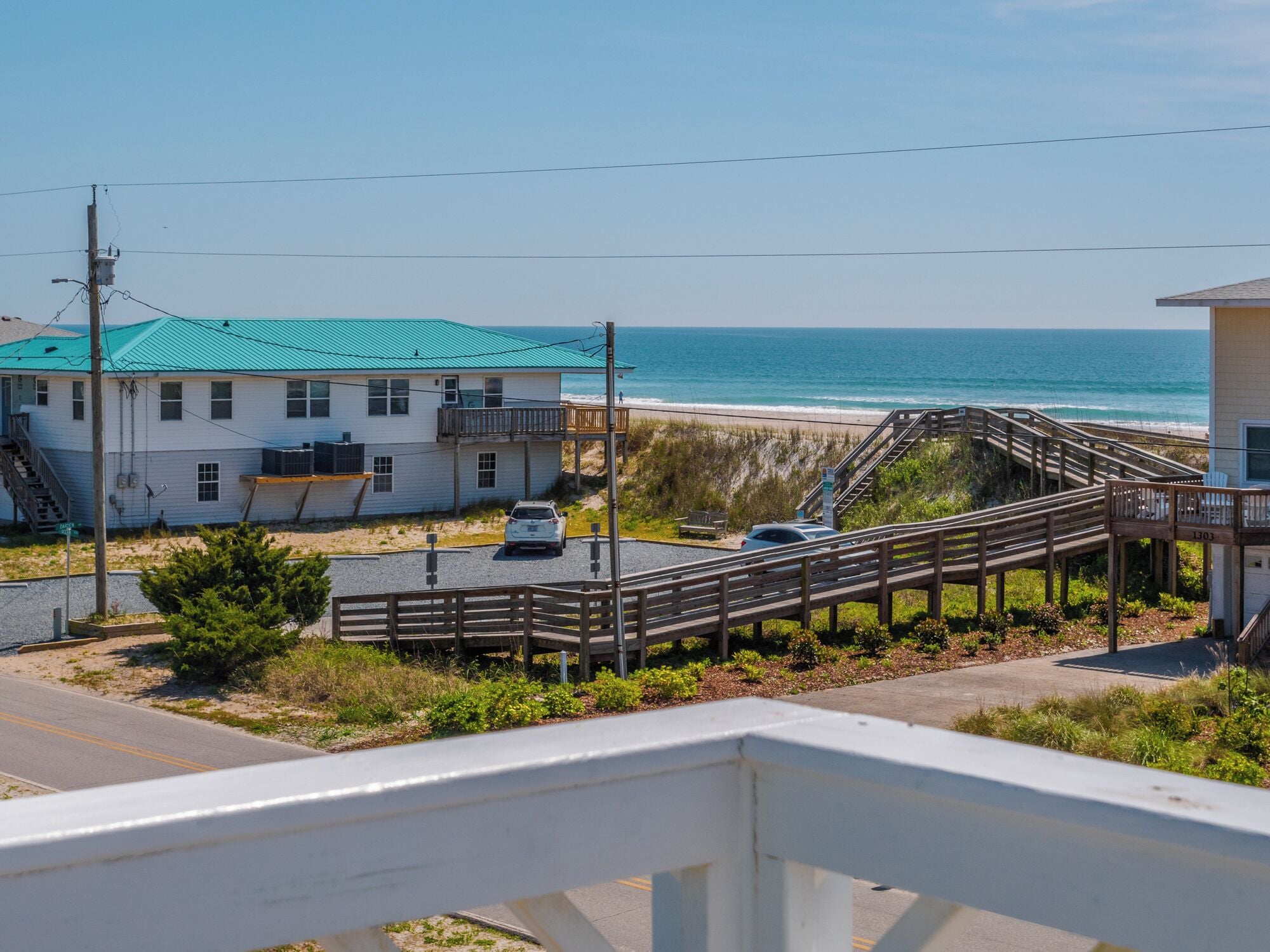 Una proprietà costiera con una terrazza in legno che conduce a una spiaggia, un edificio bianco con tetto verde e una vista libera sull'oceano.
