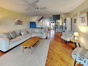 A spacious living area with a large sofa, a coffee table, and a patterned armchair. A staircase leads to an upper level.