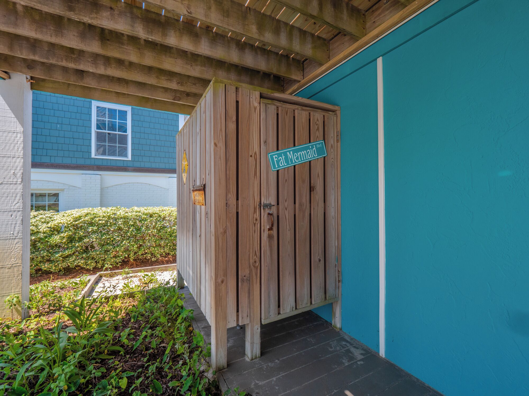 A wooden storage cabinet with a 'Fat Mermaid Blvd' sign, located under a wooden pergola with a blue wall in the background.