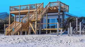 A beachfront property with a wooden staircase leading to a balcony, a large window, and a statue. - Vintage Vacation by Topsail Realty (Holly Ridge)