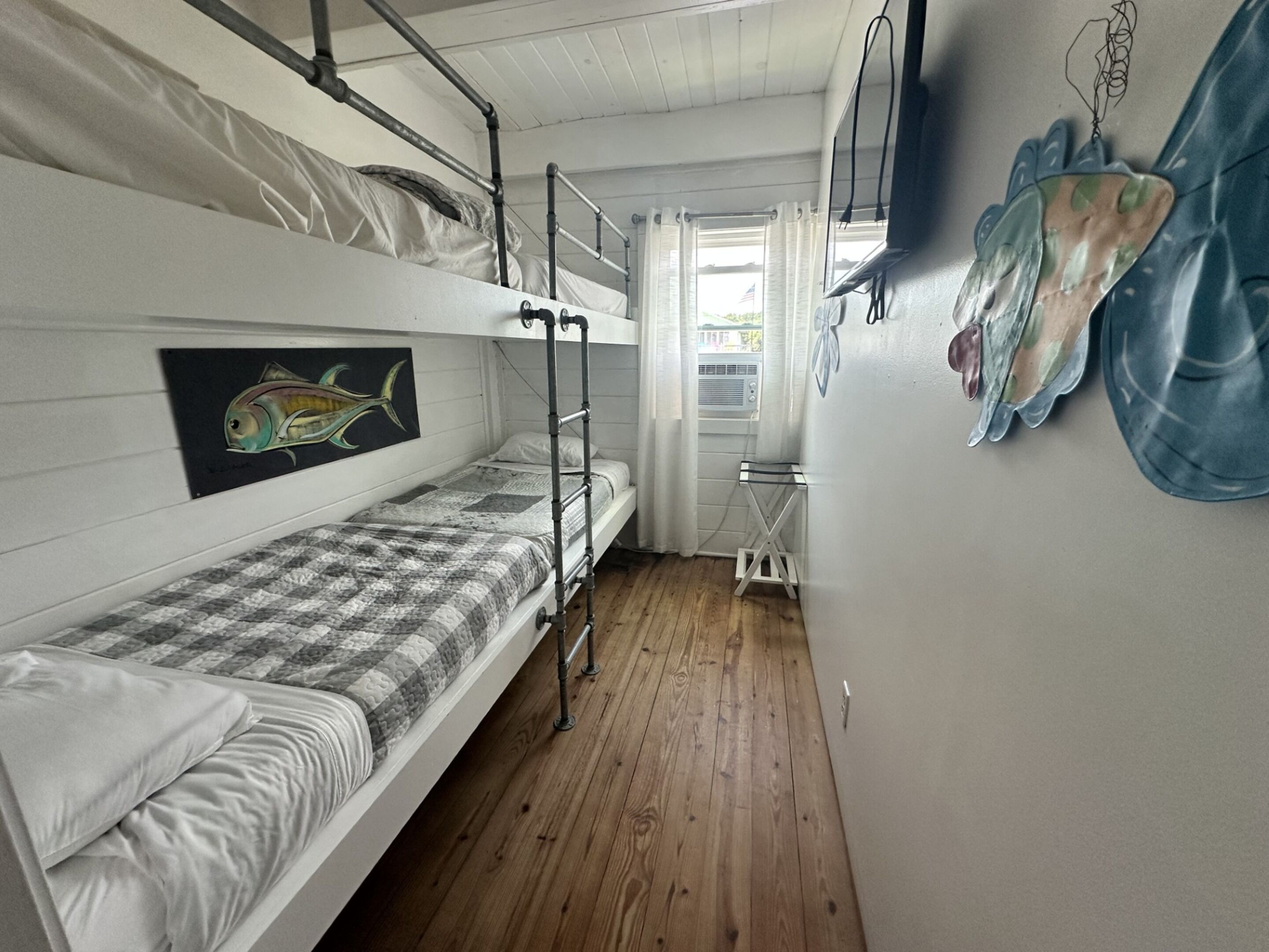 Habitación con literas, suelo de madera, una mesita y un cuadro de un pez en la pared.