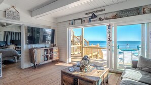 A cozy room with a wooden floor, a large TV, a wooden cabinet, and a view of the beach through a glass door. - Vintage Vacation by Topsail Realty (Holly Ridge)