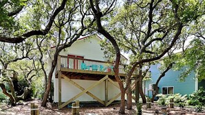 A house with a wooden deck and a covered porch, surrounded by trees and garden plants. - Sea Angels by Topsail Realty (Holly Ridge)