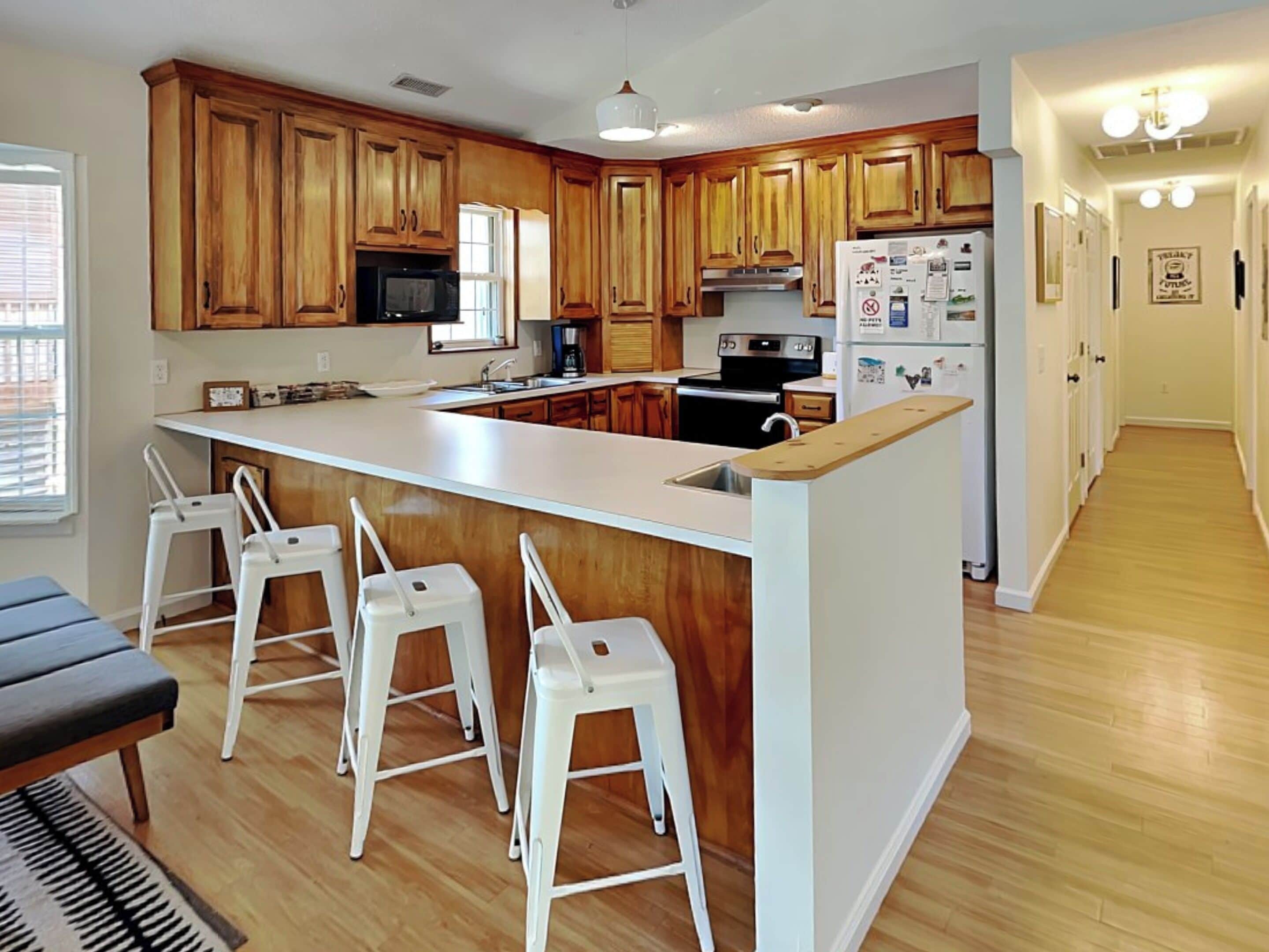 A modern kitchen with wooden cabinets, a central island with bar stools, a microwave, stove, and refrigerator.