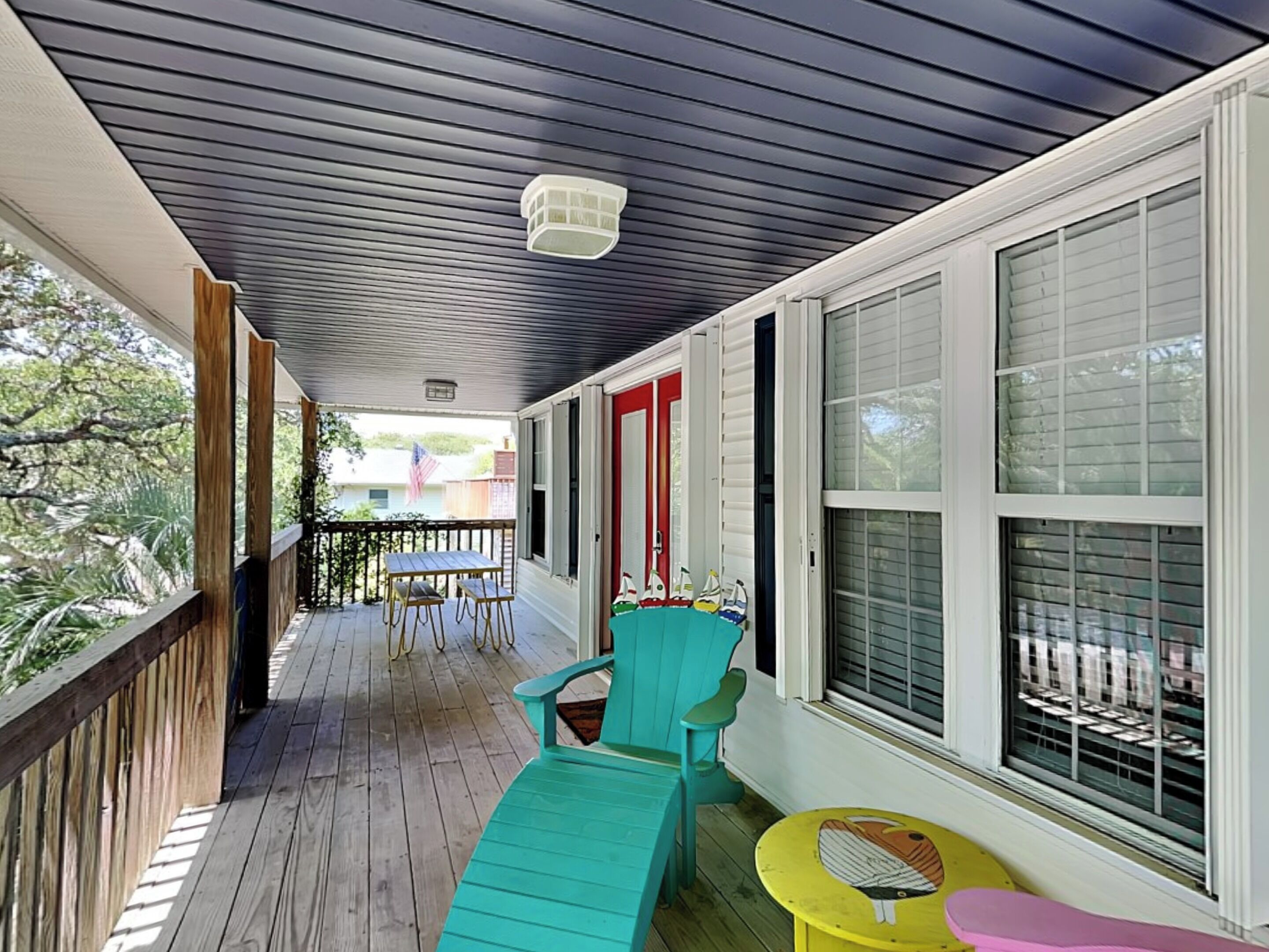 A covered porch with wooden flooring, a table, chairs, and a small table with a bird design.