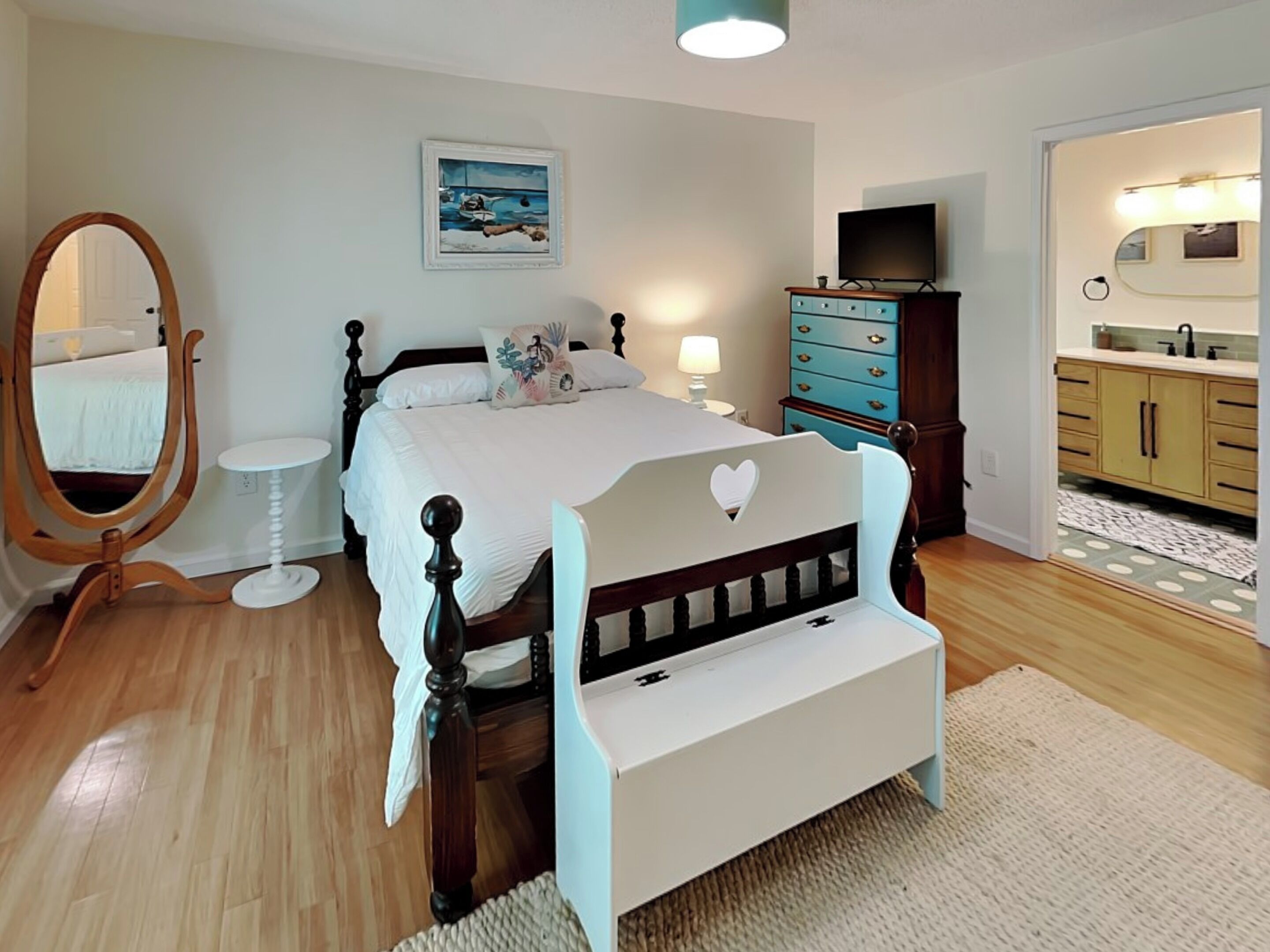A bedroom with a wooden bed, a white bedside table, a mirror, a dresser, and a television.
