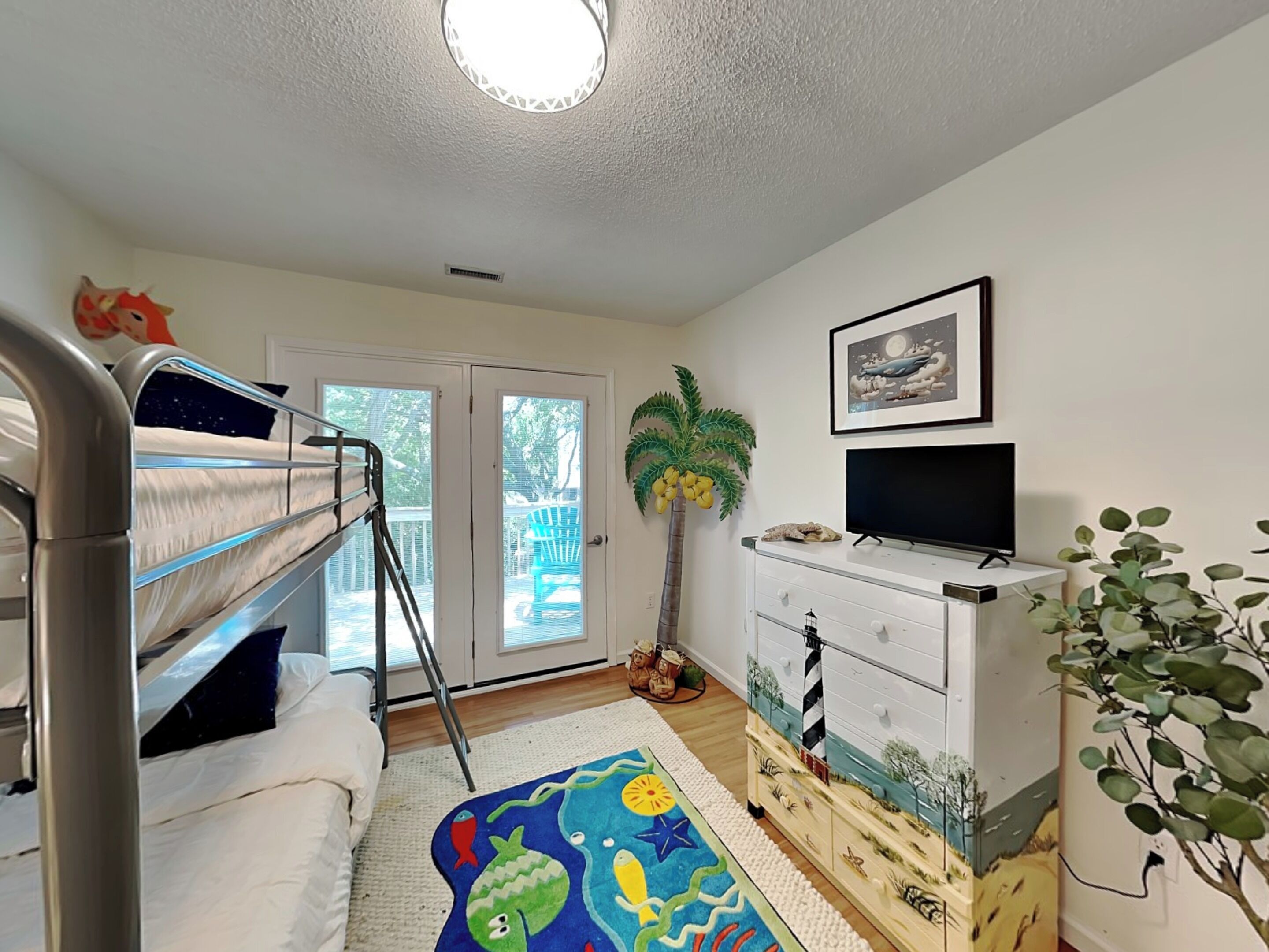 A child's bedroom with bunk beds, a dresser, a television, and a door leading to a balcony.