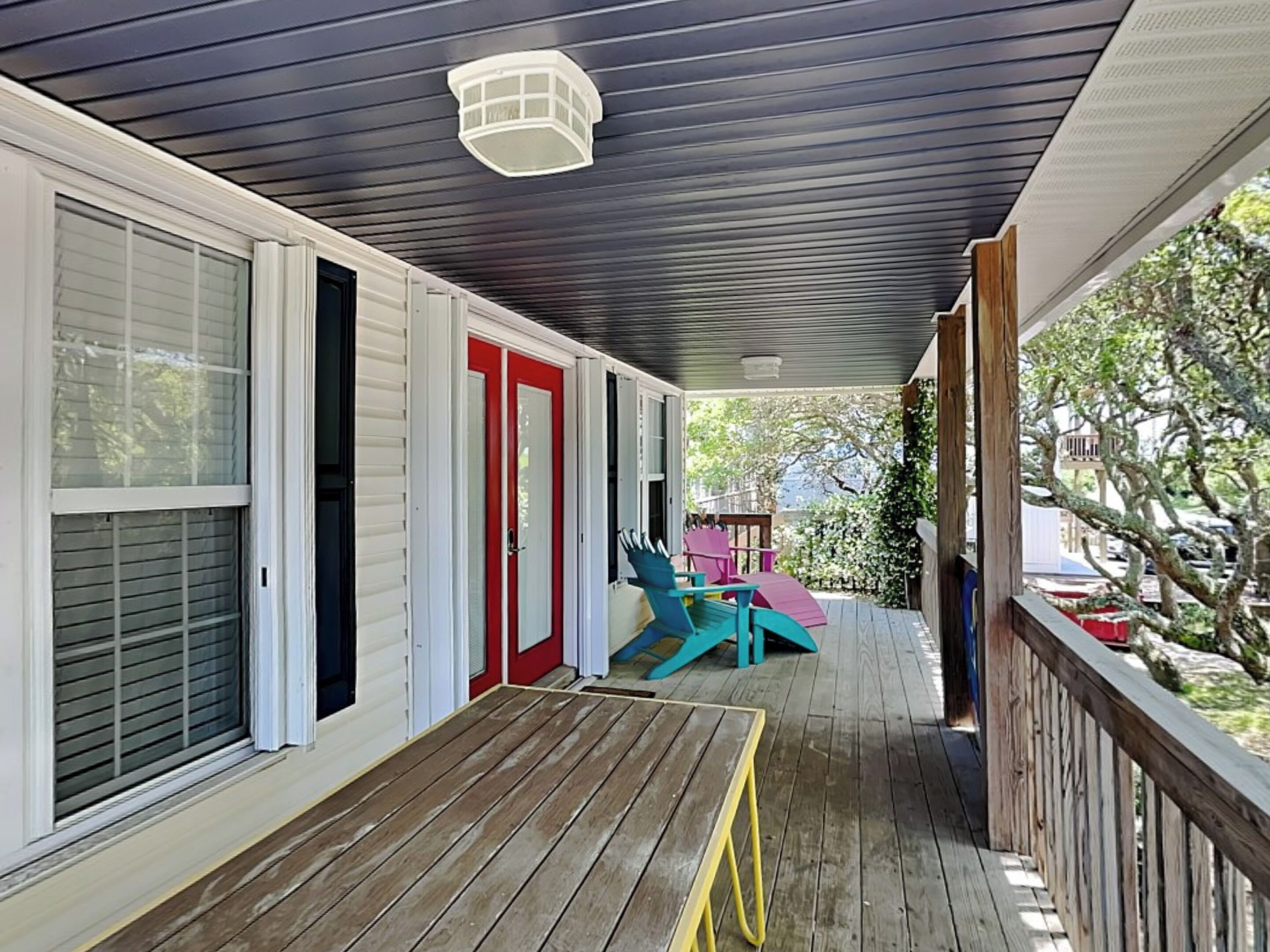 A covered porch with a wooden deck, a red door, and two turquoise chairs.