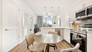 A modern kitchen with white cabinets, a stainless steel microwave, and a built-in oven. There is a dining area with a round table and patterned chairs. - Dorsen Stay (Atlanta)