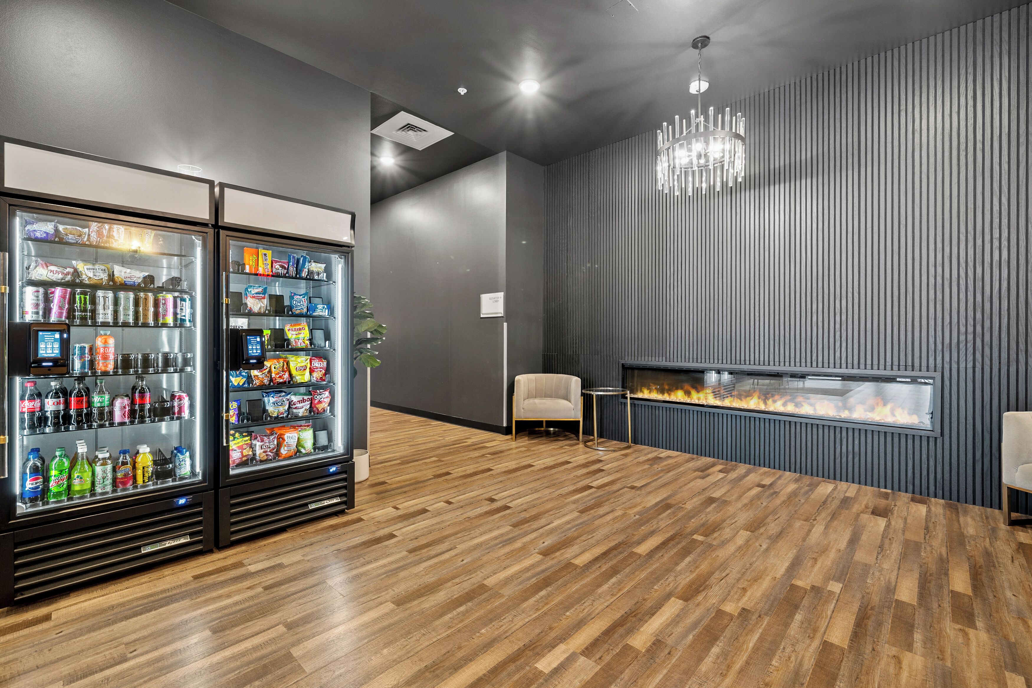 A modern lounge area with two beverage vending machines, a fireplace, and a wooden floor.