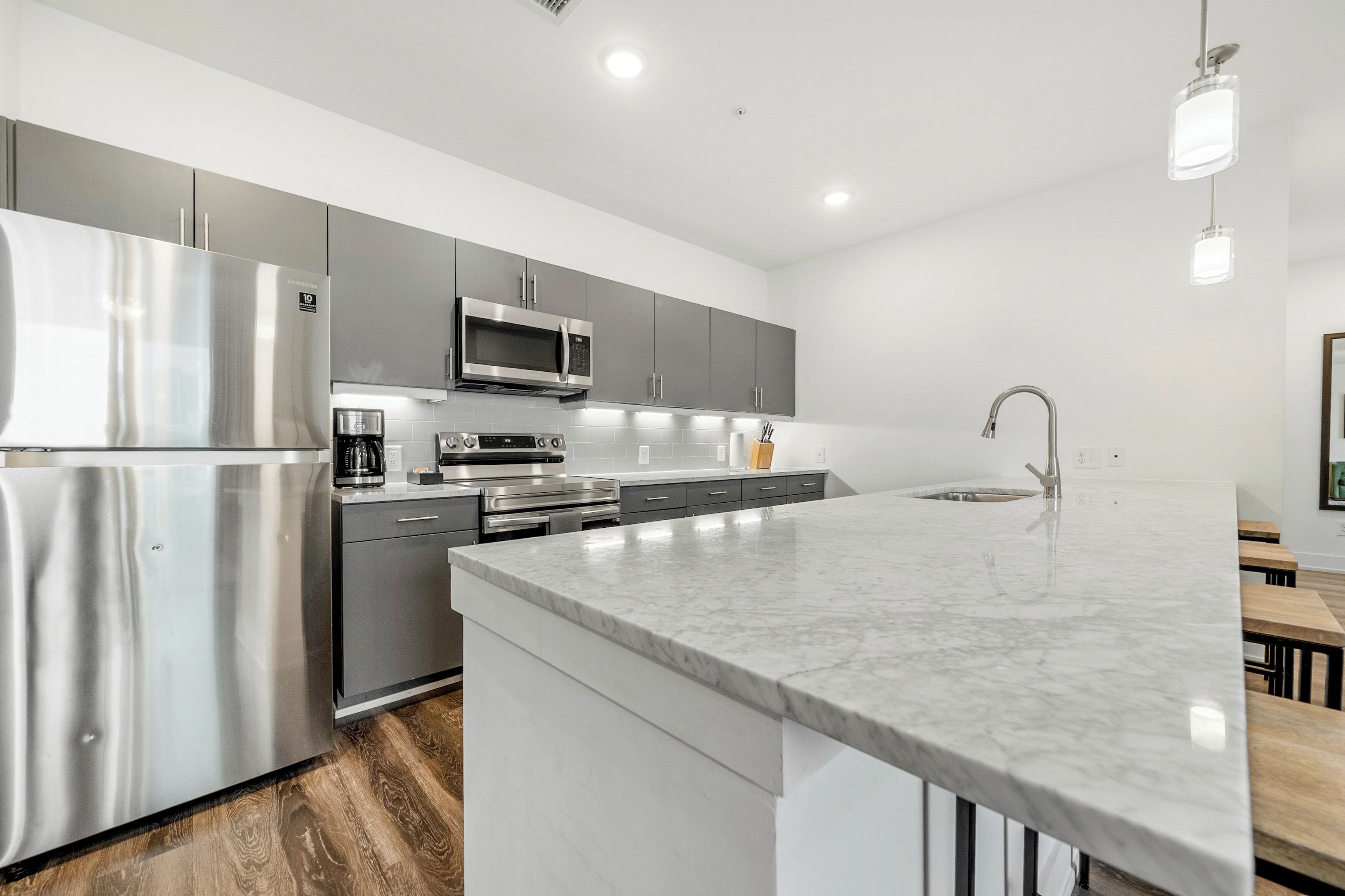 A modern kitchen with stainless steel appliances, grey cabinets, and a marble countertop.