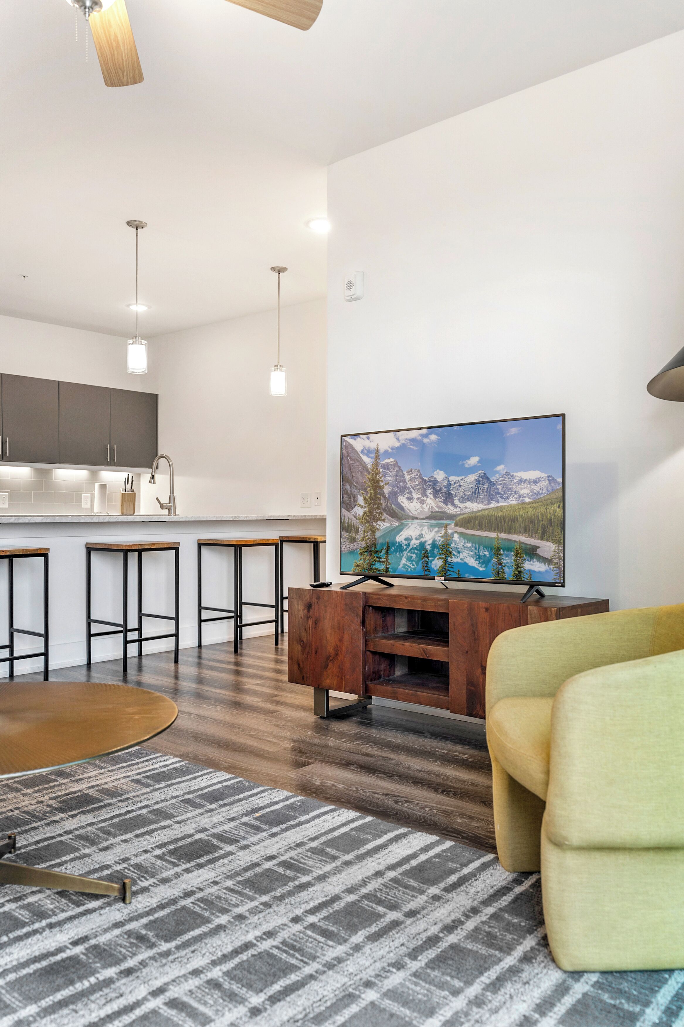A modern living room with a wooden coffee table, a yellow armchair, and a large flat-screen TV mounted on a wooden stand.