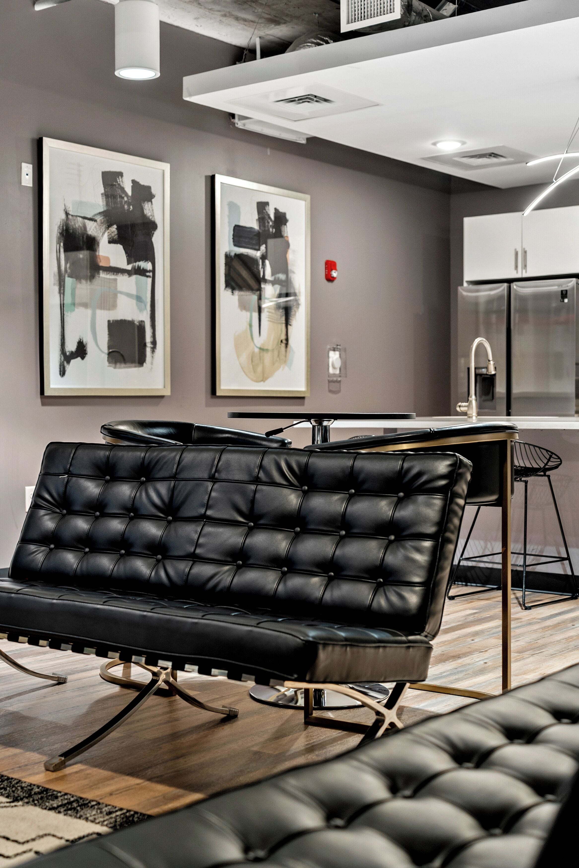 A modern room with a black leather sofa, a dining table, and two abstract paintings on the wall.