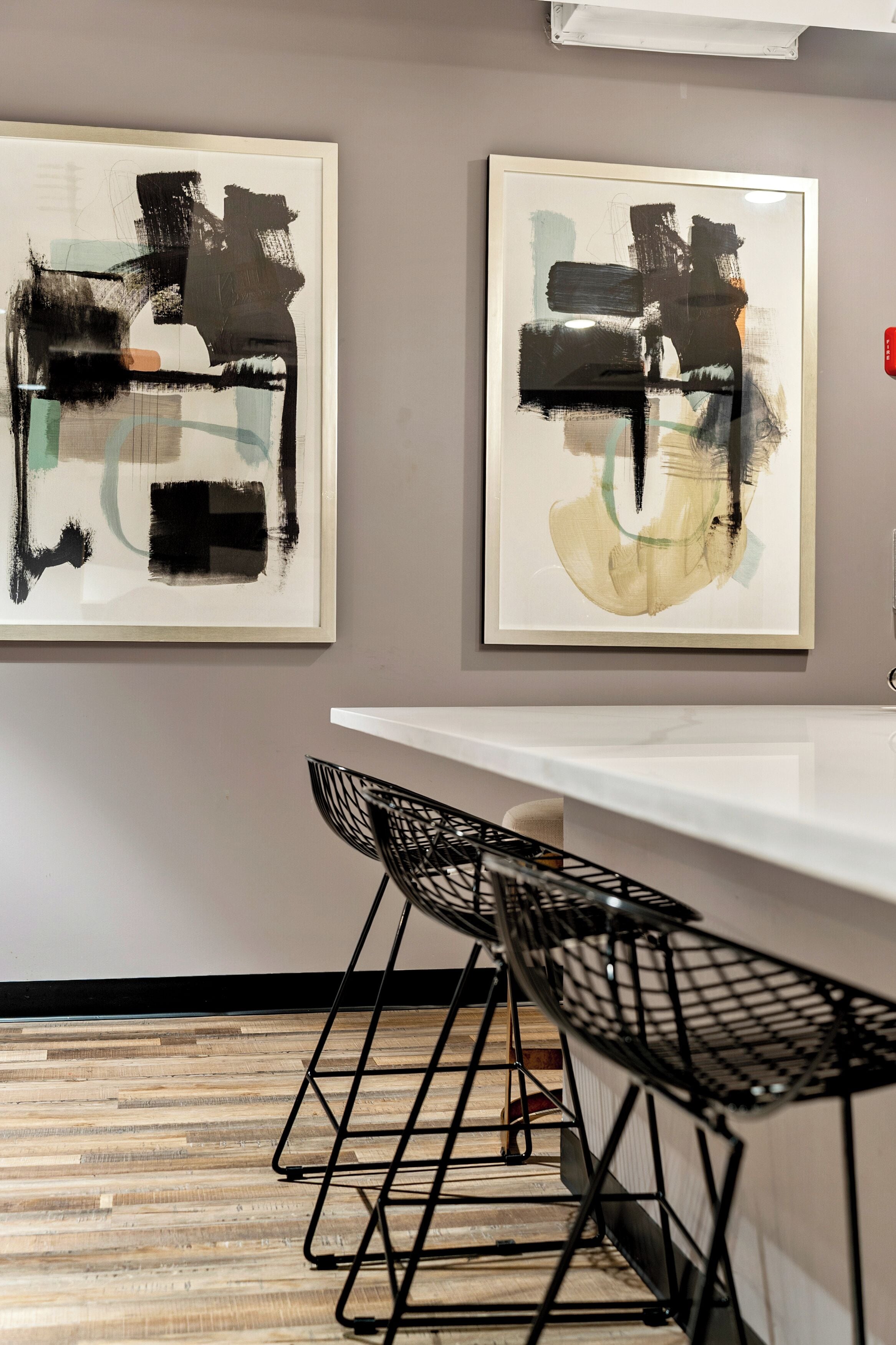 A modern interior with abstract paintings, a white table, and black wireframe chairs.