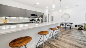 A modern kitchen with grey cabinets, a white countertop, and stainless steel appliances. There are three wooden stools and a round table with chairs. - Dorsen Stay (Atlanta)