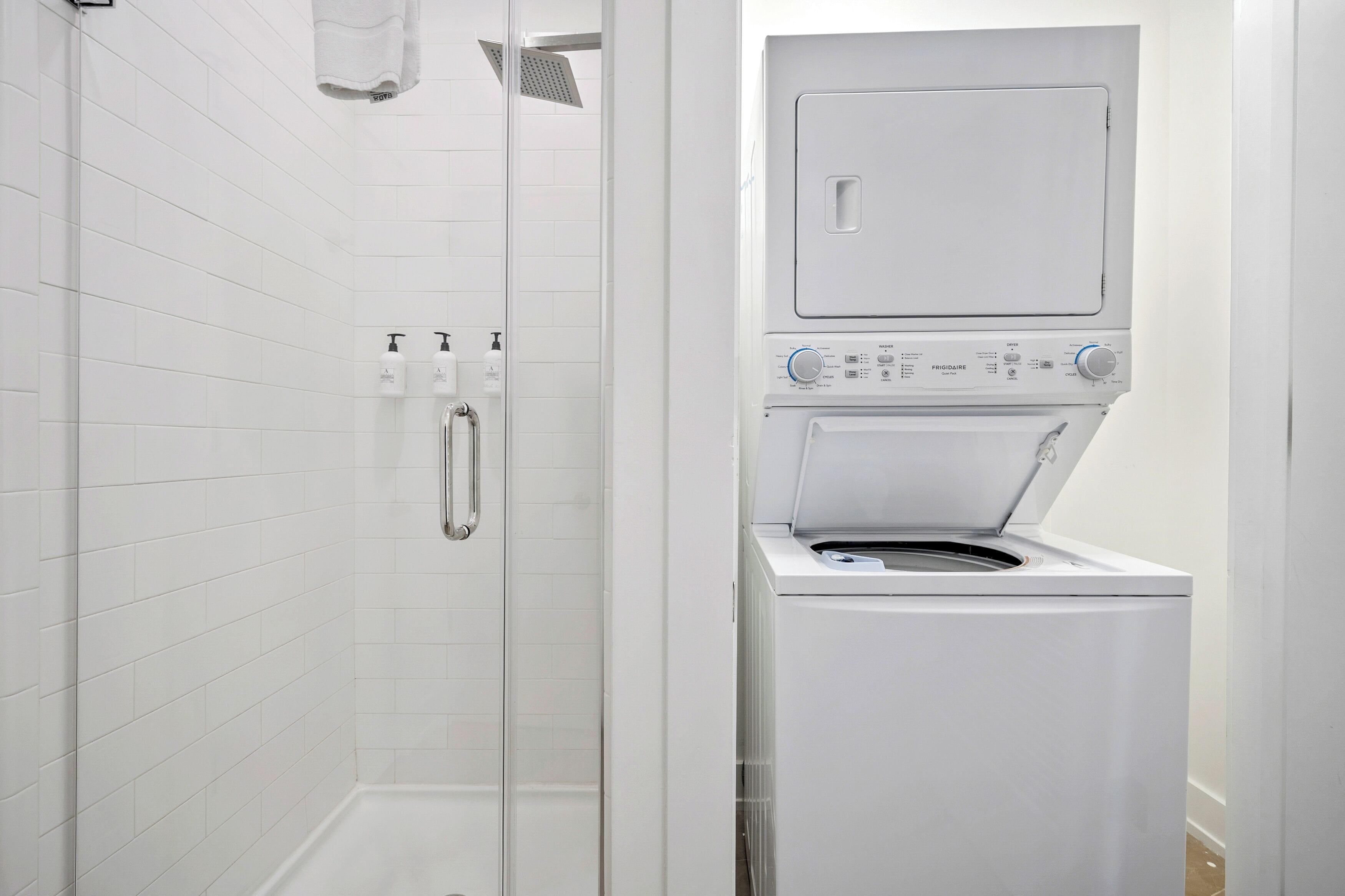 Ein modernes Badezimmer mit einer Duschkabine, einer integrierten Waschmaschine und einem Trockner sowie weißen Fliesenwänden.