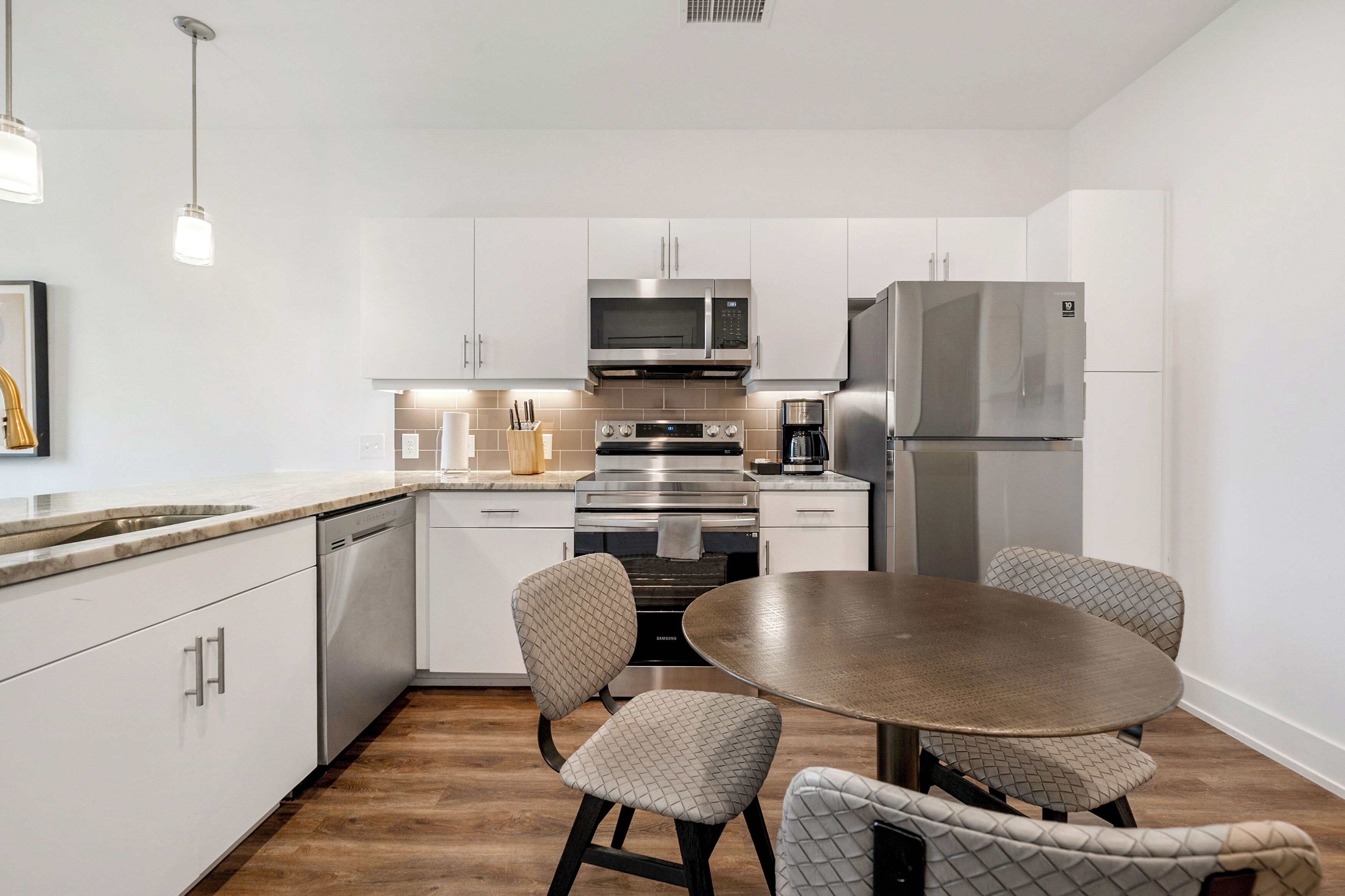 A modern kitchen with white cabinetry, stainless steel appliances, a round dining table, and patterned chairs.