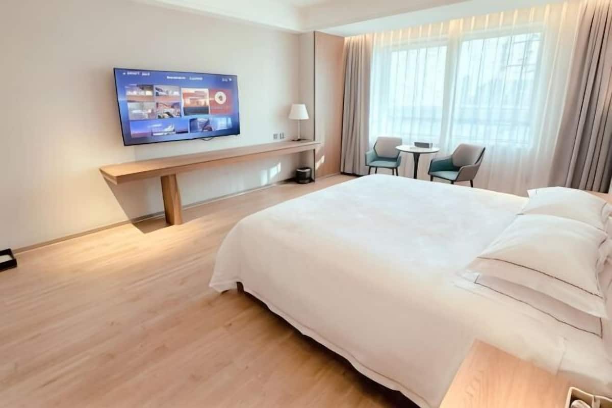 Une chambre d’hôtel avec un grand lit, un téléviseur fixé au mur, une petite table et une chaise.