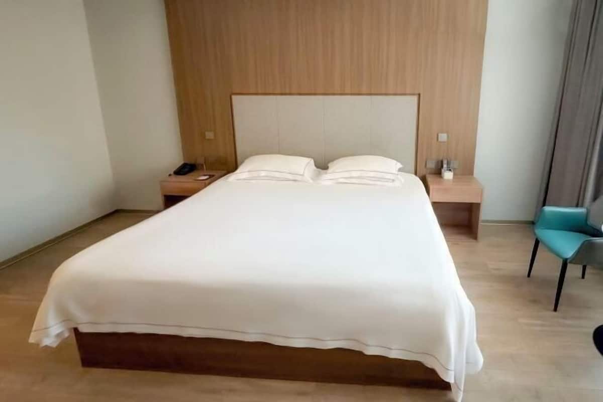 Une chambre d’hôtel avec un grand lit, une tête de lit en bois, des tables de chevet et une chaise.