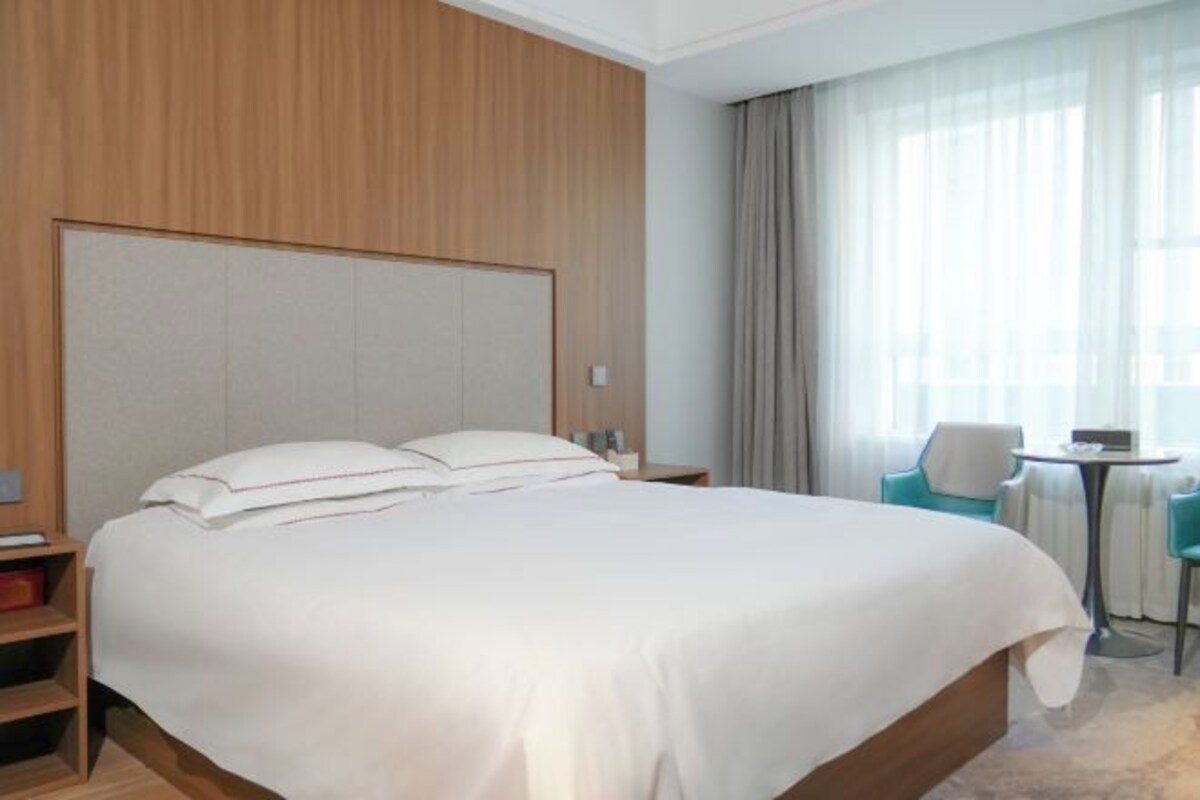 Een hotelkamer met een groot bed, een houten hoofdeinde, een klein tafeltje en een stoel.