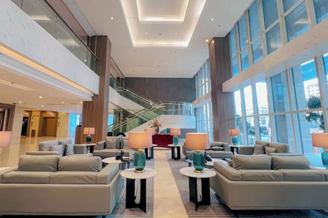 A spacious lobby with high ceilings, a central staircase, and multiple seating areas with lamps.