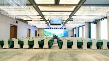 A conference room with rows of tables and chairs, a large screen at the front, and a modern ceiling design.