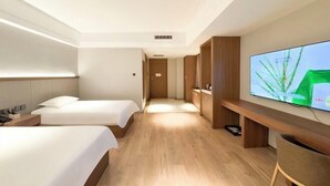Habitación de hotel con dos camas, televisor, suelo de madera y un pasillo que conduce a una puerta.