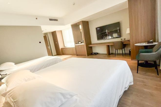A hotel room with two beds, a desk, a chair, a TV, and a small table.