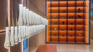 Un interior moderno con una hilera larga de luminarias únicas y texturizadas, y una pared de estantes iluminados que exhiben diversos objetos.