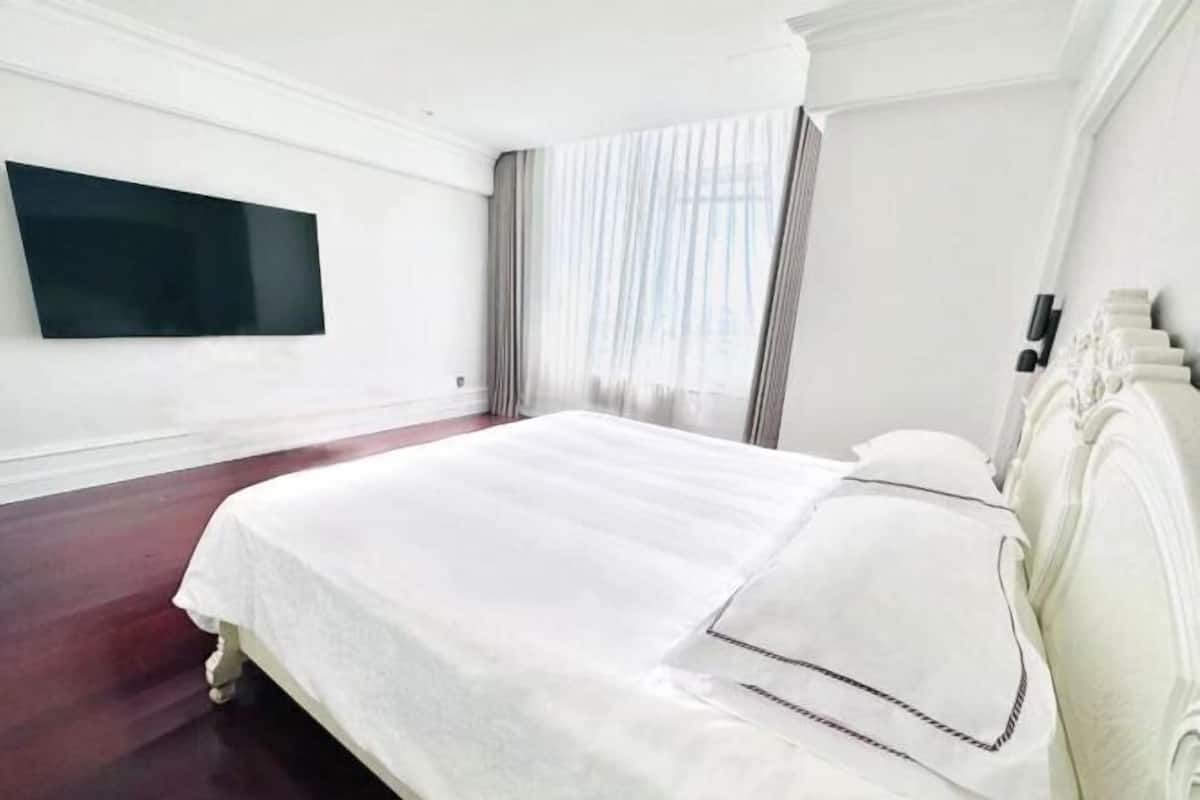 Une chambre d’hôtel avec un grand lit, un téléviseur à écran plat fixé au mur et une fenêtre avec des rideaux.