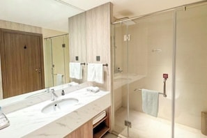 A modern bathroom with a glass-enclosed shower, a large mirror, and a marble sink.
