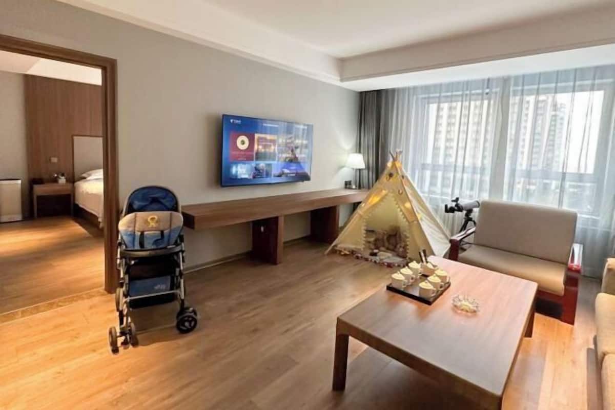 Une chambre d’hôtel avec un plancher en bois, un canapé, une table basse, une télévision, une poussette et une décoration en forme de tipi.