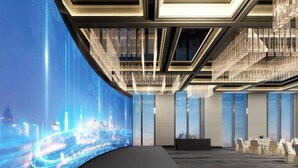 Una sala de conferencias moderna con una pared curva que muestra un paisaje urbano, ventanas amplias y una araña de cristal.