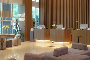 Un área de recepción moderna con un mostrador de madera, zona de estar y un ventanal grande.