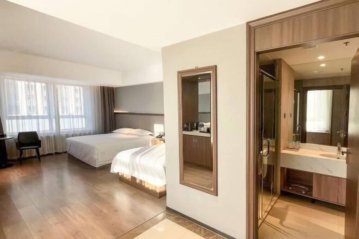 Une chambre d’hôtel comprenant un lit, un bureau, un miroir et une salle de bain avec un lavabo et un miroir.
